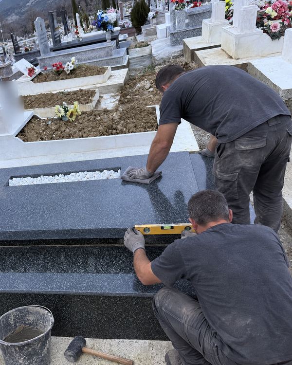 Two workers finishing a new dark granite grave